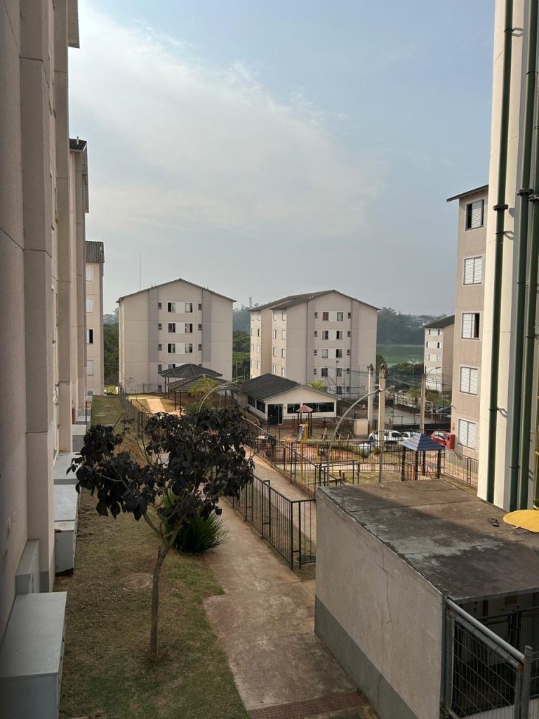 Vista de um patio entre edifícios com algumas árvores ao meio e uma área verde ao fundo.